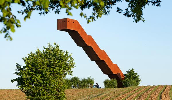 The structure appears to defy gravity. Its red-brown colour is a reference to the ironstone found locally